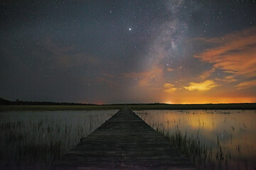 Beautiful view of the long wooden dock on the lake gleaming under the starry sky