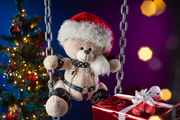 A teddy bear in a Santa Claus hat is a Christmas gift for BDSM games on the background of a...