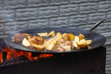 The potatoes are fried in a skillet over an open fire.