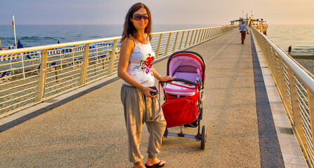 Happy woman outdoor with her newborn child inside the cradle. Motherwood concept