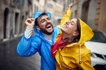 A young couple in love is excited while spending time together in a walk the city during a rainy...
