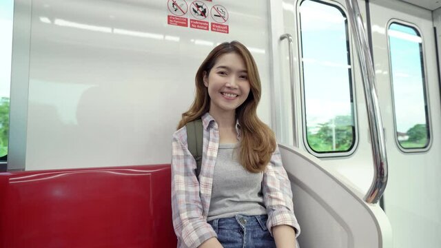 Beautiful young Asian woman enjoy traveling by train alone, sitting near windows, seeing beautiful view and smiling to camera with happiness.