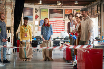 Young female colleagues race in sacks during the company's team building event