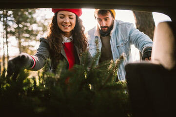 Beautiful young couple packing their christmas tree in the car going home to decorate it. 