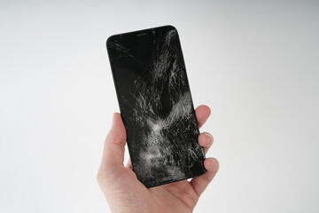 A man holds in his hand a black smartphone with broken glass on the touchscreen 