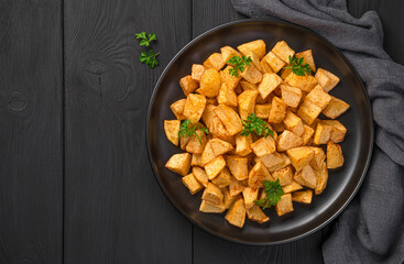 Fried potatoes with parsley on a black plate. Patatas bravas, tapas.