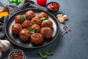 Meat meatballs in a black plate on a dark background with sauce, spices and garlic.