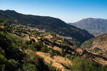 Fototapeta na wymiar Scenic view from Capileira towards Bubión and Pampaneira in the beautiful Poqueira Valley under a blue sky, Las Alpujarras, Sierra Nevada National Park, Andalusia, Spain