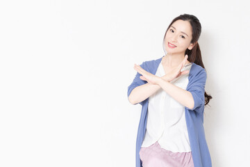 白い壁の前の椅子に座ってNGのポーズをする主婦