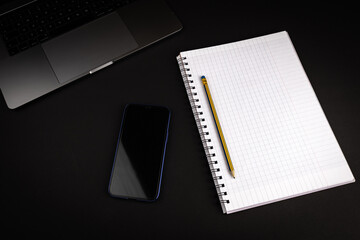 Blank notebook with pencil on black background with laptop computer and smartphone. Flat lay image for business concept.