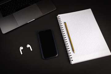 Blank notebook with pencil on black background with laptop computer and smartphone. with bluetooth headphones. Flat lay image for business concept.