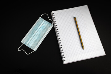 Blank notebook with pencil on black background with . Medical mask laying next to notebook. Work at home concept.