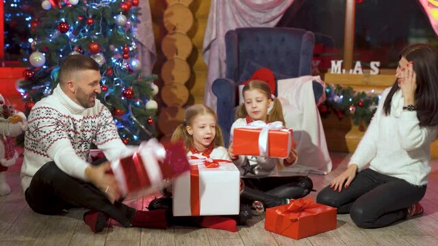 Happy family with presents at Christmas. Parents and little girls spend time together in Christmas decorated room. Children with parents put gift boxes on the floor.