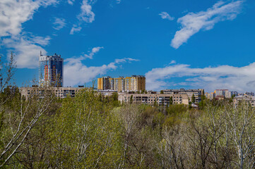 Fototapeta na wymiar Urban residential buildings on the horizon from above. City landscape. Blue sky with white clouds. The tops of the trees. Bird's-eye view. Cloudy horizon. Background image.