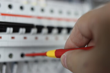 An electrical engineer uses an insulated screwdriver to connect the equipment in the control panel to control technological processes.