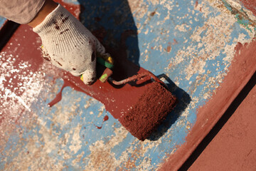 A girl paints an old metal roof with a roller