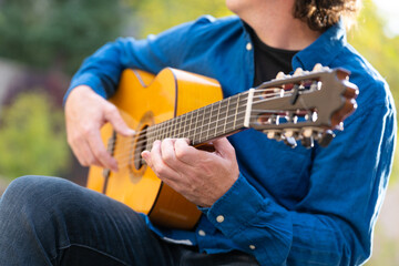 Unrecognizable middle-aged man playing Spanish guitar sitting on park bench