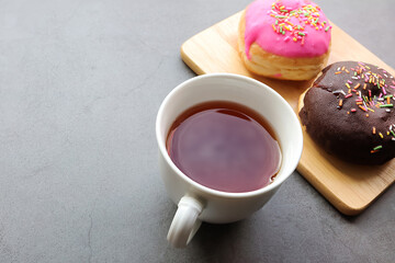 Two delicious donuts with colorful sprinkles on wooden cutting board with a cup of tea for breakfast. Top view.