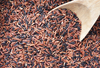 Red rice (Lady ruby grain) and Black jasmine rice in a wooden spoon on rice background.