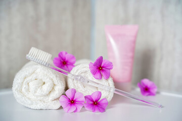 Fototapeta na wymiar Toothbrush, toothpaste and white towels, pink flowers aromatherapy. Oral care, body hygiene and morning daily routines.