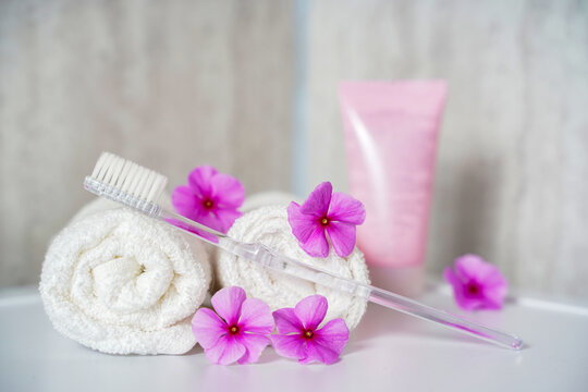 Toothbrush, toothpaste and white towels, pink flowers aromatherapy. Oral care, body hygiene and morning daily routines.