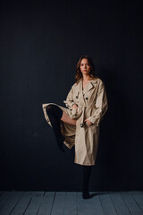 young beautiful girl in the studio on a black background, she is wearing a trench coat and black lingerie