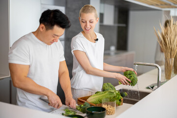 Multiracial couple cooking salad from fresh vegetables together on kitchen at home. Concept of healthy and vegetarian eating. Idea of relationship and spend time together. Asian man and european girl