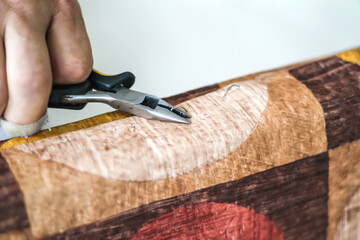 The workflow of restoration of upholstered furniture. Overworked male hands remove the old upholstery from the wooden frame of the sofa. A man, caucasian, works with flat teeth. 