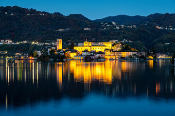 Fototapeta na wymiar Winter early sunrise panorama of Orta San Giulio island, in the same name lake (Piedmont, Northern Italy); small lake of alpine origin, is UNESCO Site and home of a cloistered nuns convent.