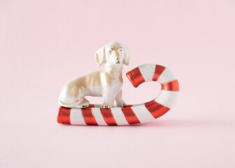 Christmas ornament red and white stick on which sits a ceramic dog figure. An unrealistic minimal New Year's concept on a pink background