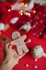 Hand holding christmas gingerbread man cookie on red festive background closeup