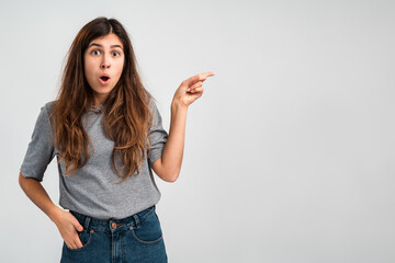 Funny woman pointing finger at copy space with surprised expression. People emotions concept. Indoor, studio shot on light white background