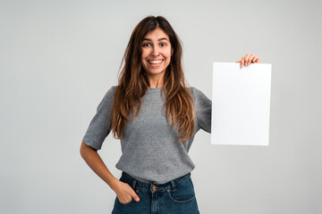 Obraz na płótnie Canvas Portrait of the caucasian overjoyed young woman holding blank paper or billboard while feeling happy isolated on white background