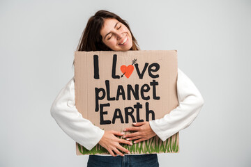 Caucasian cheerful woman embracing carton placard with signs I love planet Earth and closed her...