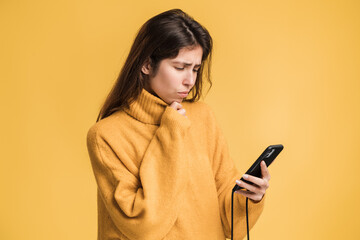 Serious brunette woman holding smartphone in hands, chatting with friends or making food order, online services. Indoor studio shot isolated on yellow background