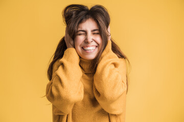 I don't want to hear. Portrait of irritated girl keeping ears closed not to listen loud annoying noise, high-decibel sound. Indoor studio shot isolated on yellow background