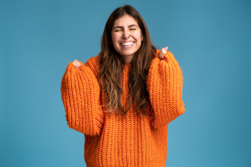 Portrait of excited overjoyed fashionably dressed woman standing with raised fists and shouting yeah, I'm winner, rejoicing victory, success. Studio shot isolated on blue background
