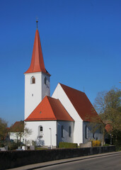 Fototapeta na wymiar Medieval village church of St Leonhard with its gothic tower, its red tile roof and a cemetery in Burgoberbach, Franken region in Germany