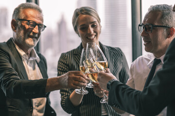 Group of  business partner celebrating their victory. Old business man making a toss to younger business man and woman. They are holding a champagne glass in a hotel lobby with city scape background.