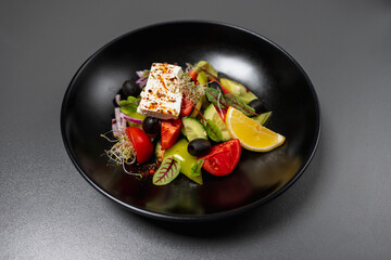 Fresh vitamin salad of vegetables. Diet salad of green peppers and cucumbers, tomatoes, olives, onions, leaves and decorated with slice of lemon, microgreen.Useful salad with piece of soft feta cheese