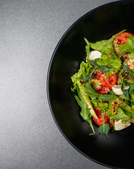 Fresh salad of organic vegetables in a plate. Restaurant food. Tomatoes, lettuce, microgreens and soft mozzarella cheese in a vitamin healthy dish. Salad smeared with green sauce with avocado and oil