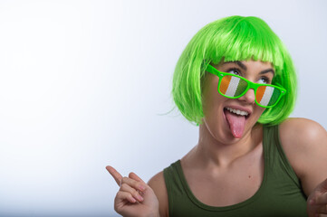 Cheerful young woman in green wig and funny glasses celebrating st patrick's day on a white...