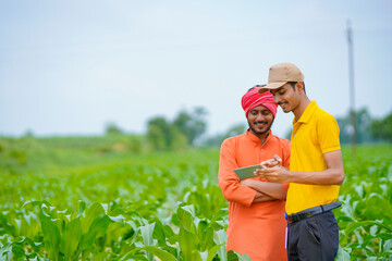 Young indian banker or agronomist showing some detail to farmers in smartphone at agriculture field.