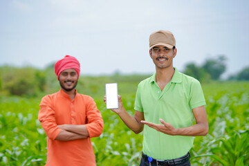 Indian agronomist showing smartphone with farmer at agriculture field.