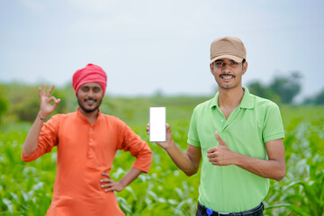 Indian agronomist showing smartphone with farmer at agriculture field.