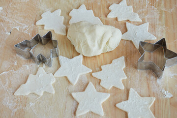 Uncooked biscuits cut with metal molds on a wooden table, sprinkled with flour. Making homemade cookies for Christmas.