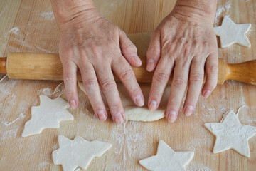 Female hands roll out dough for homemade cookies with a rolling pin on a wooden table sprinkled with flour