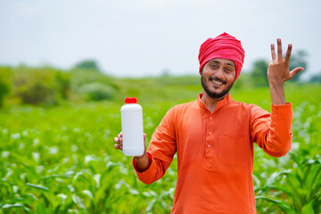 Young indian farmer showing liquid fertilizer bottle at agriculture field.