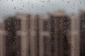Macro raindrops on window with cityscape in the afternoon with grey sky. Blurred urban skyline background with water drops. Rainy season concept.