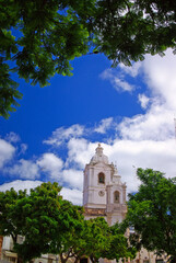 Fototapeta na wymiar A church in portuguese town, against blue cloudy sky, framed by green tree branches